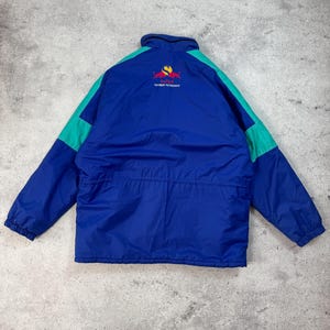 Pu&ograve; includere: Giacca blu e verde acqua con logo e testo sul retro. La giacca ha una chiusura a zip e un collo alto. Il logo &egrave; rosso e giallo. Il testo sul retro della giacca recita "SAUBER PETRONAS".