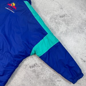 Pu&ograve; includere: Giacca vintage blu e verde acqua con logo Red Bull Sauber Petronas. La giacca presenta un design a blocchi di colore con dettagli verde acqua sulle maniche e un colletto nero. Realizzata in materiale leggero.