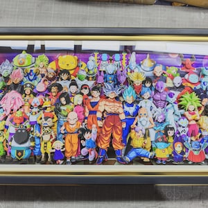 以下が含まれることがあります： ドラゴンボールのキャラクターが多数描かれた額装されたアートワーク。鮮やかな色彩の様々なキャラクターが、紫と青の背景に配置されています。フレームは黒色で、内側の縁は金色です。