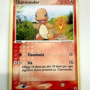May include: A vintage Charmander Pokémon trading card. The card features an orange Charmander character with a flame on its tail, set against a background of a grassy field. The card has text in Italian, including "Fiammata" and "Ira."