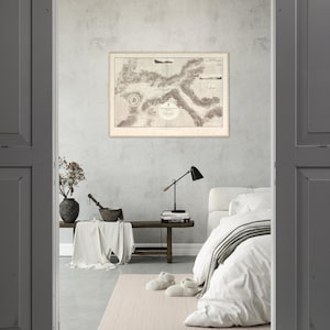 May include: A sepia-toned vintage map in a frame is displayed on a light grey wall. The map shows detailed coastlines and geographical features. A black desk lamp and a bench with decor are in the foreground, creating a cosy interior scene.