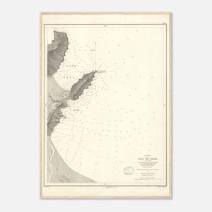 May include: A framed vintage nautical chart, featuring a detailed map of a coastal area. The chart is in grayscale, with landmasses depicted in shaded relief and the sea filled with numerous small markings. The title "PLAN DE TOLLO" is visible.