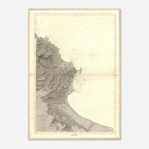 Puede incluir: Antigua carta náutica de una zona costera, enmarcada en madera clara. El mapa presenta sombreado topográfico detallado de la tierra y el mar, con numerosas marcas y una rosa de los vientos. La carta está impresa en tonos grises y beige.