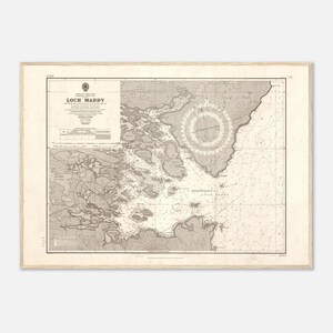 May include: A framed nautical chart of Loch Maddy, with the title prominently displayed. The chart features detailed coastlines, depths, and navigational aids in shades of gray and white. The frame is a light wood color.