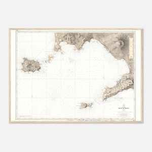 May include: A framed vintage nautical chart of the Gulf of Naples, Italy, in sepia tones. The map features detailed coastlines, islands, and sea depths, with grid lines and text labels. The frame is a light wood color.