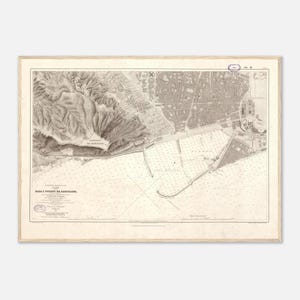 May include: Antique nautical chart of the Barcelona harbor and surrounding areas, framed in a light wood. The map features detailed depictions of the coastline, city layout, and sea depths, rendered in sepia tones. The title "Rada y Puerto de Barcelona" is visible.