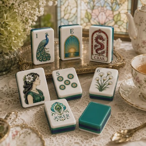 May include: A set of white rectangular mahjong tiles featuring colorful illustrations including a peacock, a sunrise, a red dragon with the text CRAK, a woman with flowers in her hair, a number five, a number six, and a peacock feather Joker tile.
