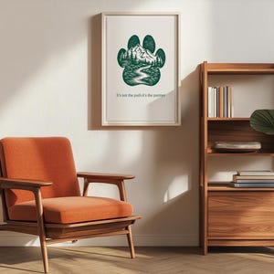 May include: A framed print with a green paw print design, depicting a mountain and river scene. The text "It's not the path it's the partner" is below. An orange armchair and wooden bookshelf are also visible in the room.