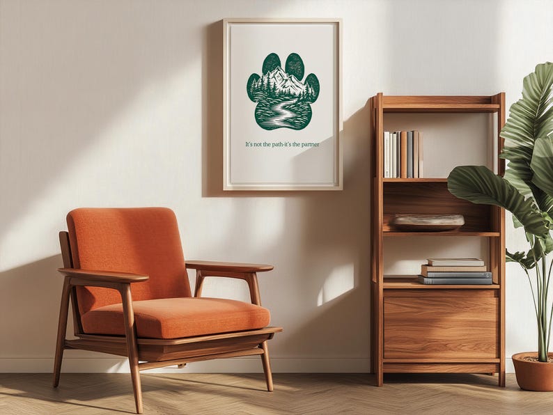 May include: A framed print with a green paw print design, depicting a mountain and river scene. The text "It's not the path it's the partner" is below. An orange armchair and wooden bookshelf are also visible in the room.