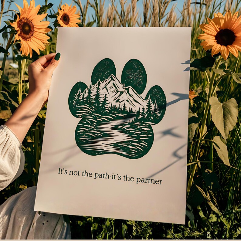 May include: A white poster with a green paw print design, depicting a mountain and forest scene. The text "It's not the path-it's the partner" is printed at the bottom. The poster is held in a field of sunflowers.