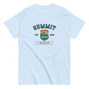 K&ouml;nnte beinhalten: Hellblaues T-Shirt mit einem grafischen Design. Das Design zeigt das Wort "SUMMIT" in gr&uuml;nem, bogenf&ouml;rmigem Text &uuml;ber einer Berg- und Sonnenuntergangsgrafik. Darunter steht "DENVER SUMMIT CO." und "8088". Das Wort "DENVER" ist rot gedruckt.