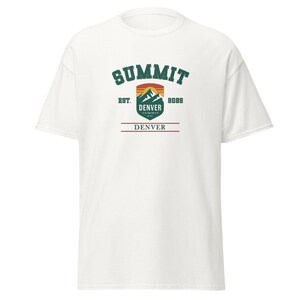 K&ouml;nnte beinhalten: Wei&szlig;es T-Shirt mit einem gr&uuml;nen, orangefarbenen und braunen Aufdruck. Der Aufdruck enth&auml;lt das Wort "SUMMIT" &uuml;ber einem Berg und das Wort "DENVER" darunter. Das Shirt hat auch den Text "EST. 8088".