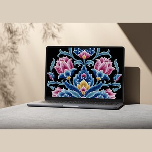 May include: A silver laptop displays a floral design on its screen. The design features pink, blue, and yellow flowers with intricate details against a black background. The laptop is on a gray surface.