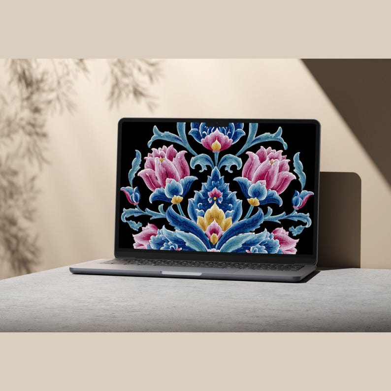 May include: A silver laptop displays a floral design on its screen. The design features pink, blue, and yellow flowers with intricate details against a black background. The laptop is on a gray surface.