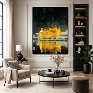 May include: A framed print of the Golden Temple in Amritsar, India, at night, reflected in the water. The print is in a modern living room with neutral tones, a black side table, and a beige armchair.
