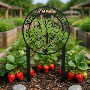 Könnte beinhalten: Ein schwarzer Metall-Gartenstecker mit den Worten "Strawberry Patch" in einem kreisförmigen Design. Der Stecker zeigt eine ausgeschnittene Illustration von Erdbeeren und Blättern. Der Stecker befindet sich in einem Gartenbeet mit Erdbeerpflanzen und reifen roten Erdbeeren.