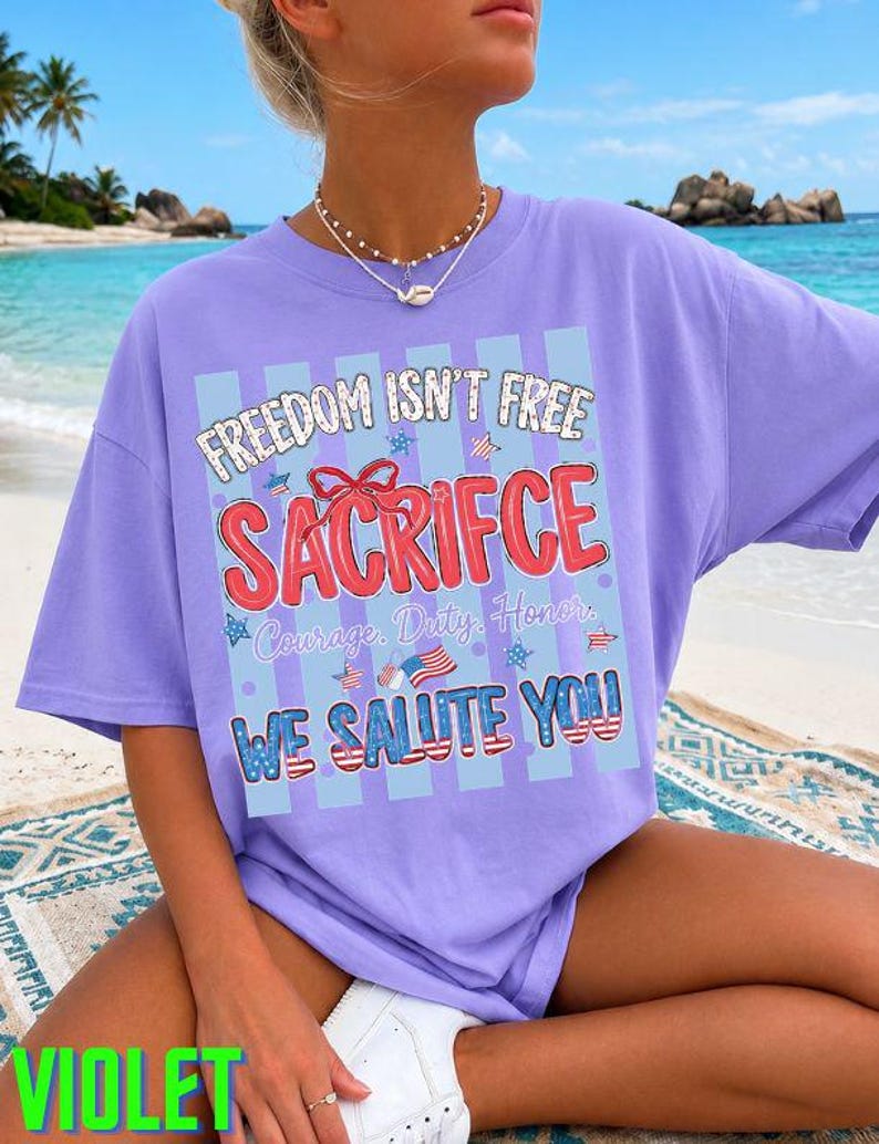 May include: A violet-colored t-shirt with the text "FREEDOM ISN'T FREE SACRIFICE" in red, white, and blue. The shirt also features the words "Courage, Duty, Honor" and "WE SALUTE YOU". The word "VIOLET" is printed in green at the bottom.