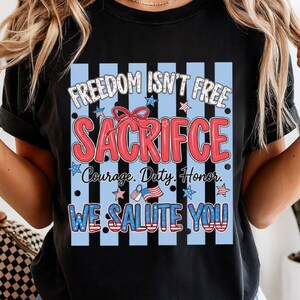 May include: Black t-shirt with a patriotic design. The design includes the text "FREEDOM ISN'T FREE SACRIFICE Courage. Duty. Honor. WE SALUTE YOU" in red, white, and blue. The design is set against a blue and white striped background.