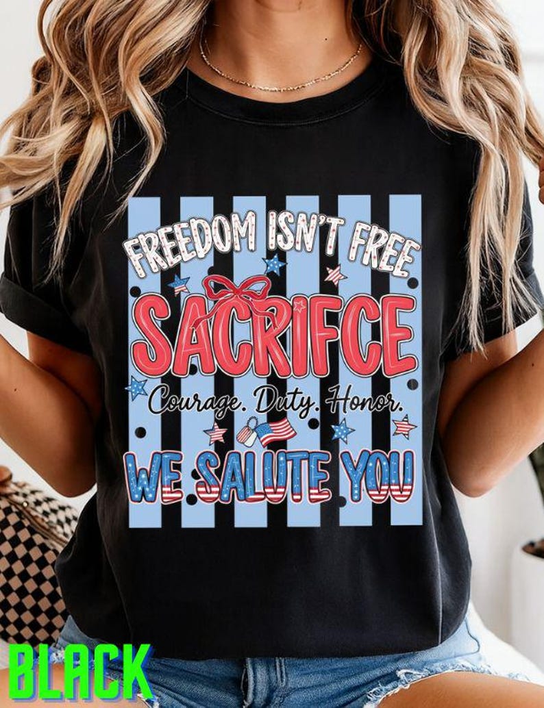 May include: Black t-shirt with a patriotic design. The design includes the text "FREEDOM ISN'T FREE SACRIFICE Courage. Duty. Honor. WE SALUTE YOU" in red, white, and blue. The design is set against a blue and white striped background.