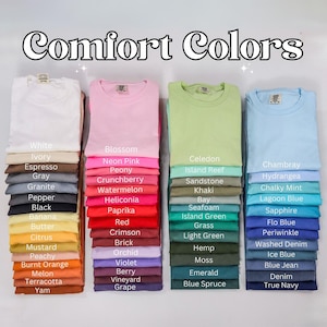 May include: Stacks of Comfort Colors t-shirts in various colors, including white, pink, green, and blue. Each stack displays a folded t-shirt with a color name label. The image features the text "Comfort Colors" at the top.