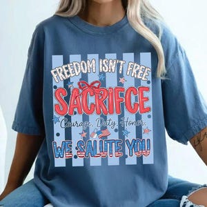 May include: A blue t-shirt with the text "FREEDOM ISN'T FREE SACRIFICE Courage. Duty. Honor. WE SALUTE YOU" in red, white, and blue. The shirt has a patriotic theme with stars and stripes.