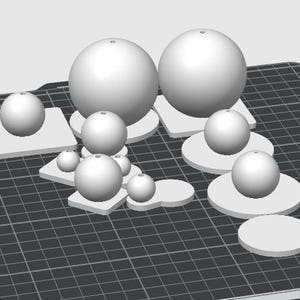 May include: A digital 3D rendering of multiple white spheres of varying sizes, each mounted on a flat base. The spheres are arranged on a dark gray grid surface, with some bases being square and others circular, all featuring a small hole at the top.