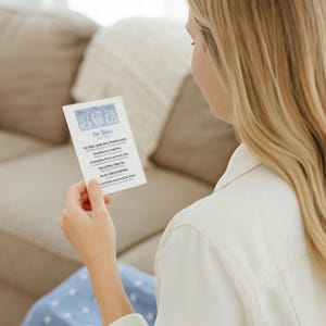 May include: A white card with the text "Ave Maria" and religious text in a script font. The card has a blue decorative border at the top. The card is held by a person with long blonde hair.