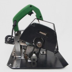May include: A black and silver Nomex brand tile cutter with a green handle. The power tool has a black blade guard and a silver base. The cord is black.