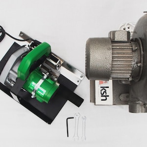 May include: An industrial air blower with a green and silver saw, black power cord, and a set of wrenches. The blower is metallic gray with a cylindrical motor and a rounded housing.