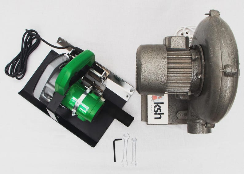 May include: An industrial air blower with a green and silver saw, black power cord, and a set of wrenches. The blower is metallic gray with a cylindrical motor and a rounded housing.