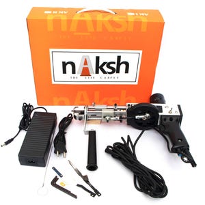 May include: An orange box with the text "nAksh THE LIFE CARPET" and a rug tufting gun with accessories. The gun is black and silver, with a handle and a power supply. Additional tools and a black cord are also included.