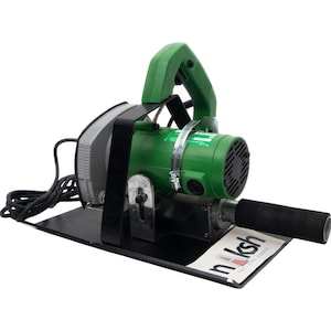 Op de afbeelding: Een groen en grijs elektrisch gereedschap met een zwarte basis en handvat. De tool heeft een zwart snoer en een label met de tekst "naksh the life carpet". De tool is ontworpen voor het snijden van tapijt.