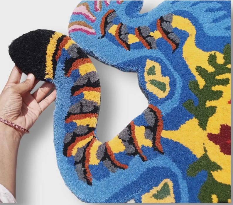 May include: A colorful, abstract rug with a unique shape. The rug features a vibrant mix of blue, yellow, black, orange, and green. The design appears to be hand-tufted, with a soft, textured surface. The rug's irregular shape adds to its artistic appeal.