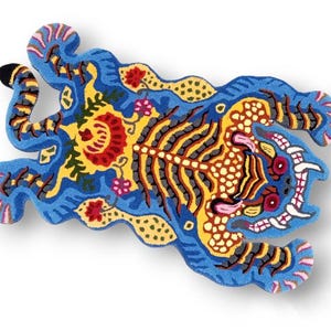 May include: A vibrantly colored rug in the shape of a tiger. The rug features a blue background with yellow, red, and black details. The tiger's body is adorned with intricate patterns and floral motifs, creating a decorative piece.
