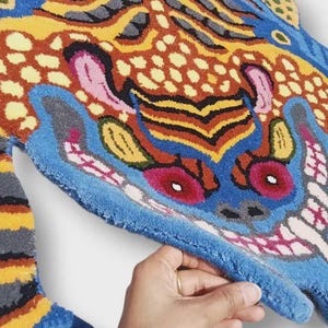 May include: A colorful, patterned rug with a unique design. The rug features a vibrant mix of blue, orange, yellow, and pink hues. The rug's design is abstract, with a focus on bold shapes and contrasting colors. The rug is made of a soft, textured material.