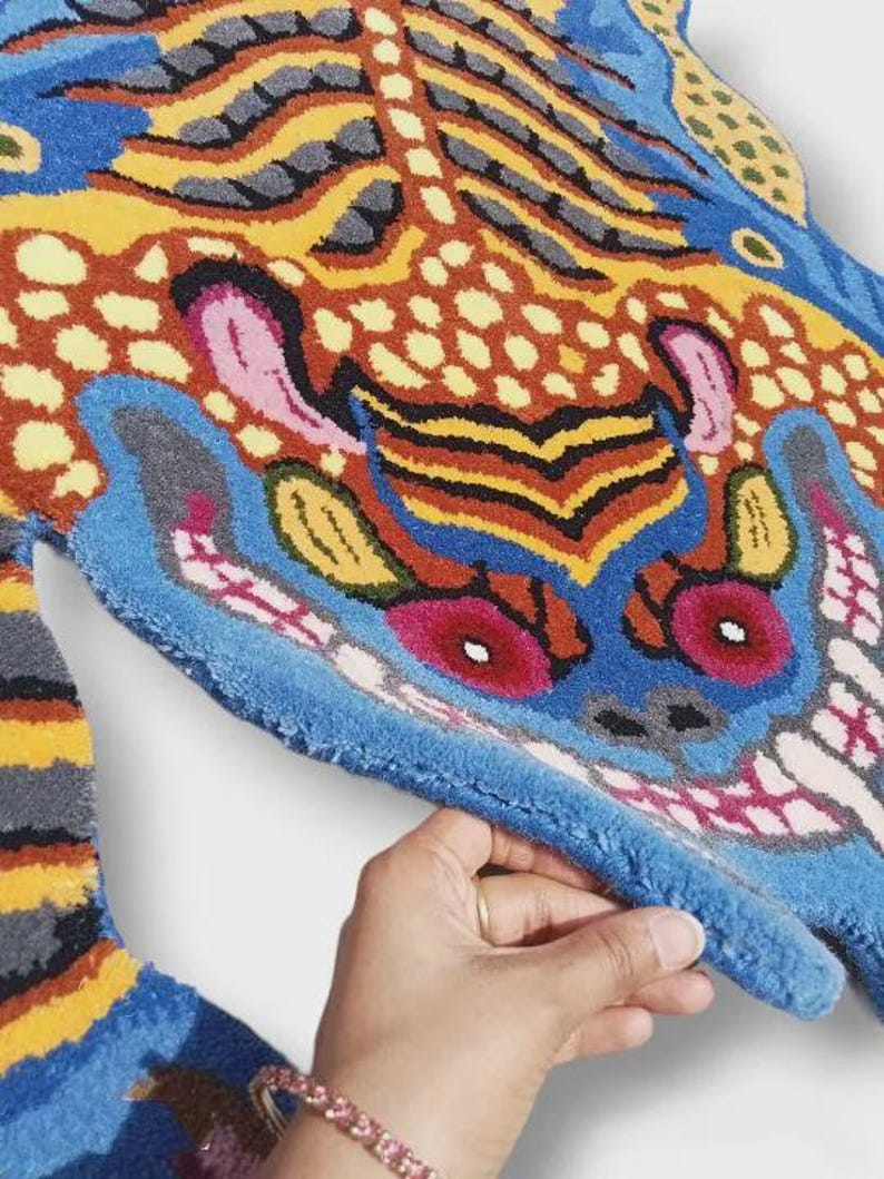 May include: A colorful, patterned rug with a unique design. The rug features a vibrant mix of blue, orange, yellow, and pink hues. The rug's design is abstract, with a focus on bold shapes and contrasting colors. The rug is made of a soft, textured material.