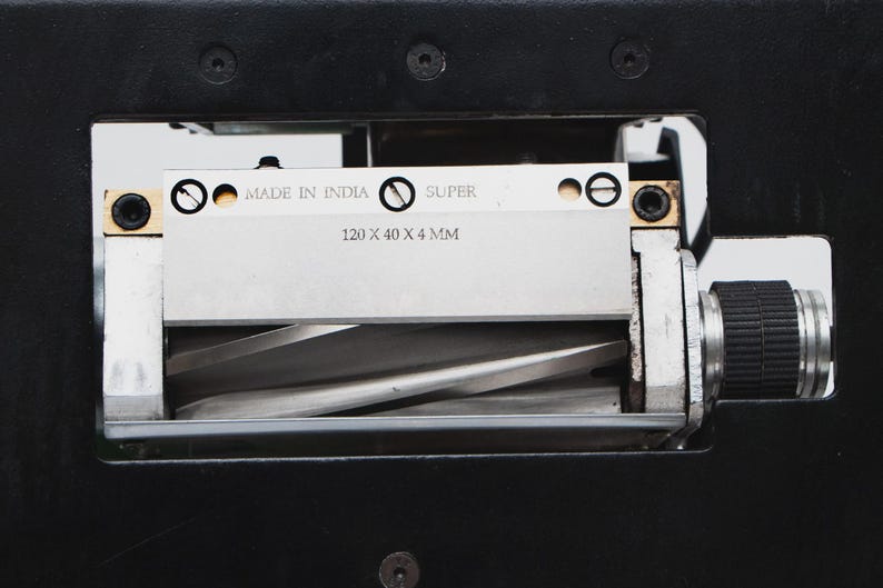 May include: Close-up of a metal blade assembly with the text "MADE IN INDIA" and "SUPER". The blade measures 120 x 40 x 4 mm. The assembly is set in a black metal frame.