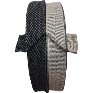 May include: Two rolls of decorative ribbon. One roll is black with a textured pattern, and the other is beige with a herringbone design. The ribbons are likely used for crafts, sewing, or gift wrapping.