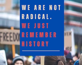 May include: A blue sign with white and red text that reads "WE ARE NOT RADICAL. WE JUST REMEMBER HISTORY." The sign is held up in a crowd of people, with other signs visible in the background.