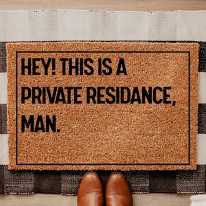 May include: A rectangular doormat with the text "HEY! THIS IS A PRIVATE RESIDANCE, MAN." in black letters. The mat is brown with a black border and is placed on a black and white checkered rug. Brown leather shoes are at the bottom.