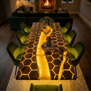 May include: A rectangular wooden dining table with a honeycomb pattern and a glowing yellow river of resin. The table is surrounded by green velvet chairs. A vase of flowers and a small statue are on the table. The table is the focal point of a dining room.