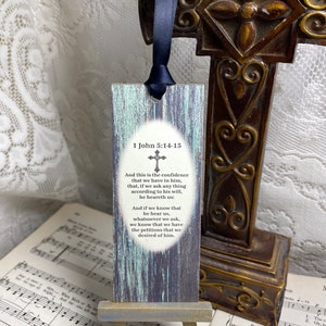 May include: A wooden bookmark with a distressed blue and green paint finish. It features a cross and the text "1 John 5:14-15" and a bible verse about faith and prayer.