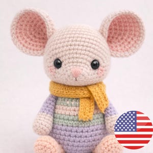 Könnte beinhalten: Eine handgefertigte Häkelmaus-Puppe mit großen, rosa gefütterten Ohren, schwarzen Augen und einer rosa Nase. Die Maus trägt einen gelben Schal und einen gestreiften Pullover in Pastellfarben. Ein charmantes, weiches Spielzeug.