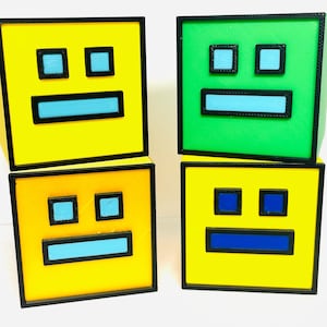 May include: Four colorful, geometric cube-shaped objects. Two are yellow, one is green, and one is orange. Each cube features a black outline with blue and black rectangular shapes resembling a face. The cubes are stacked.
