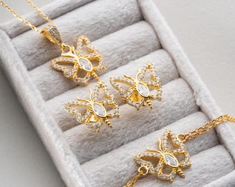 May include: A gold-colored jewelry set featuring butterfly designs. The set includes a necklace, earrings, and a bracelet. Each piece has a butterfly pendant with clear, sparkling stones and a central, larger stone.