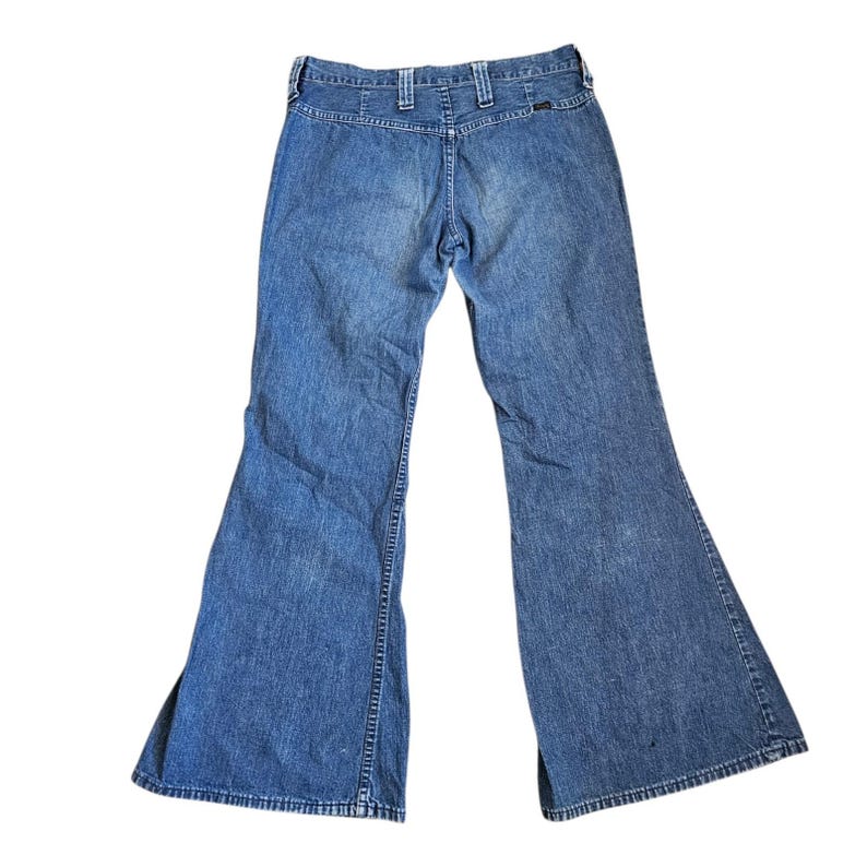 May include: Light blue denim bell-bottom jeans. The jeans have a high waist and a flared leg design. The back of the jeans is visible, showing the belt loops and pockets. The denim has a faded appearance.