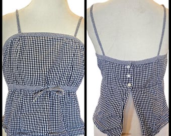 May include: A black and white gingham print camisole top with thin straps and a bow detail at the waist. The top has a square neckline and a split back with button closures. The trim is a contrasting gingham pattern.