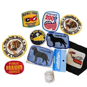 May include: A collection of vintage embroidered patches featuring various designs, including a bowling alley, a dog, a Labrador, a war memorial, and a public service logo. The patches are colorful and have a variety of textures.