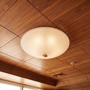 May include: A round, flush-mount ceiling light fixture featuring a frosted white glass shade with a delicate, etched lattice pattern. The center of the dome is secured by a small, circular metallic gold-toned knob, providing a clean, bright glow.