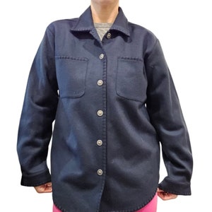May include: A navy blue button-down shirt with two front pockets and silver buttons. The shirt has a collar and long sleeves with dark cuffs. The fabric appears to be a soft, warm material, suitable for cooler weather.